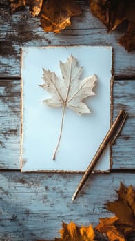 A delicate white maple leaf rests on textured paper next to an antique pen on a weathered wooden table covered in autumn leaves.