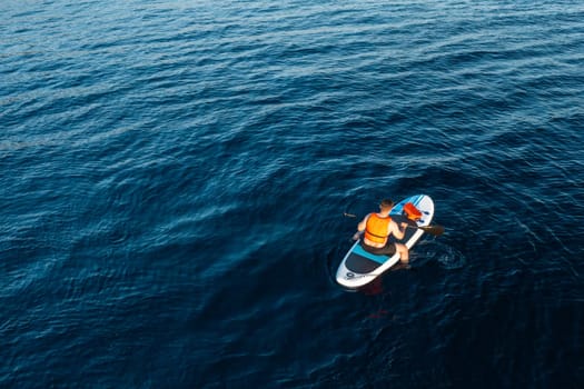 Aerial view of man sitting on the SUP surrounded by the breathtaking blue of the azure sea