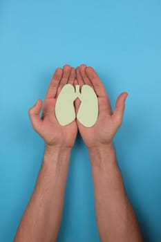 Women's hands hold a paper lungs symbol on blue background. Concept of World Tuberculosis Day or healthcare and diagnostic from covid, pneumonia or donation organ