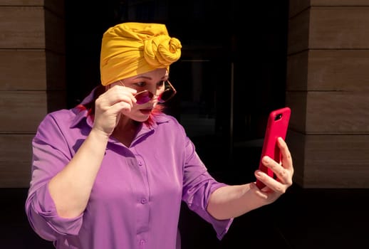 Happy and funny cool lady with fashionable clothes on dark background look to the phone with different emotions - adult asian with extravagant style, concepts about lifestyle, fasion and elderly people.