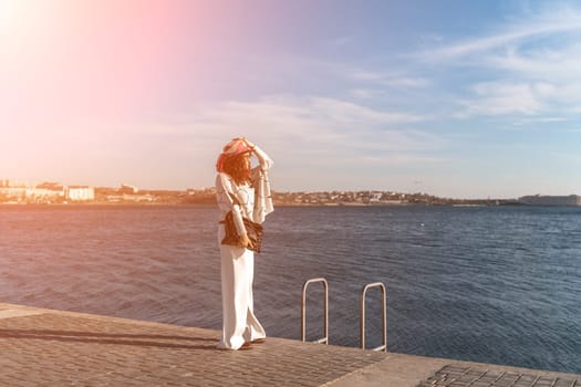 Stylish seashore woman. Fashionable woman in a hat, white trousers and a light sweater with a black pattern on the background of the sea