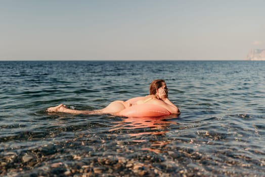 A woman is floating on a pink inflatable raft in the ocean. The water is calm and the sky is clear. The woman is enjoying her time in the water
