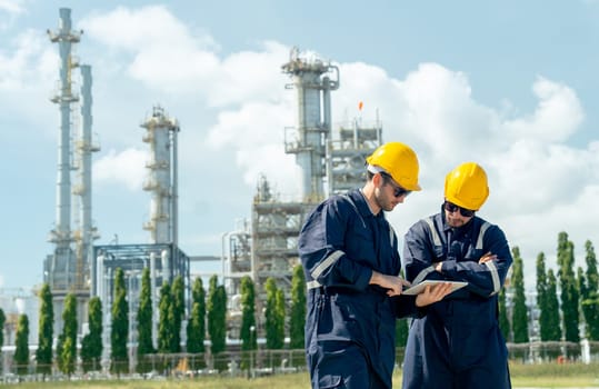 Two factory engineer or technician workers discuss together with tablet and stand in front of refining and petrochemical factory with day light.