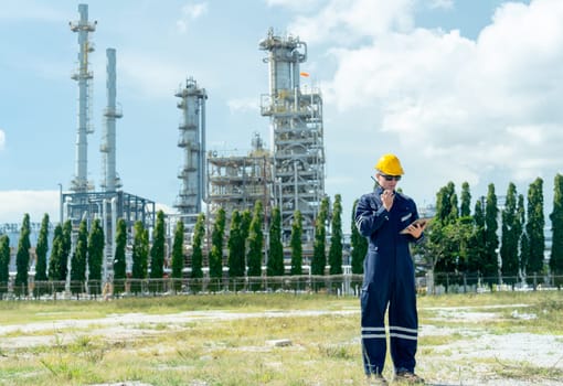 Wide shot of factory engineer or technician worker man hold walkie-talkie to discuss with coworker and stand in front of refining and petrochemical factory with day light.