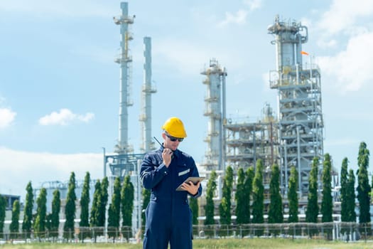 Factory engineer or technician worker man hold walkie-talkie to discuss with coworker and stand in front of refining and petrochemical factory with day light.
