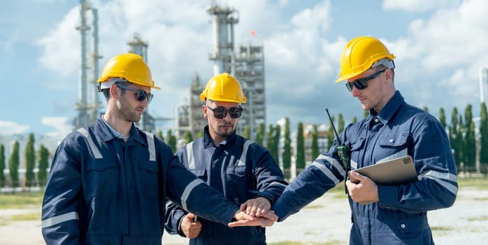 Close up factory engineer or technician workers stand and join hands together in front of refining and petrochemical factory with day light.