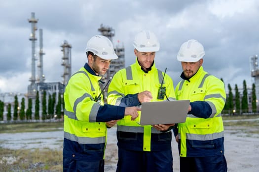 Group of engineer or technician workers stand in front of  petrochemical factory and use laptop to discuss their work.