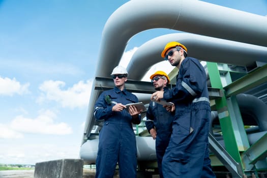 Side view of engineer or factory technician worker team stand under petrochemical gas pipeline with one also point to the pipeline in workplace.