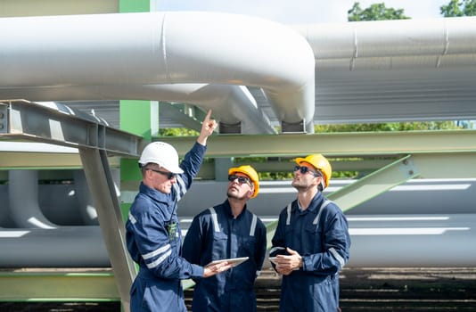 Group of engineer or factory technician worker team stand under petrochemical gas pipeline with one also point to the pipeline in workplace.