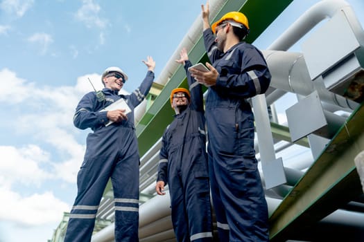 Group of engineer or factory technician workers stand beside petrochemical gas pipeline and raise hands up to express the happiness about the success of their work.