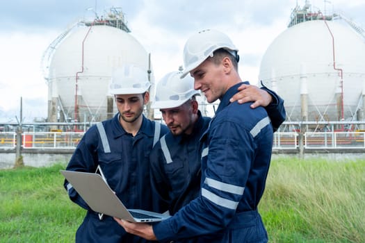 Engineer or technician workers stand and look to laptop and stand in front of petrochemical factory with cloudy sky.