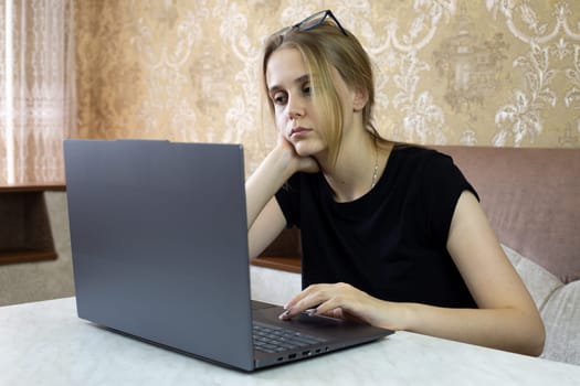 Pensive girl is trying to solve work problem and thinks while sitting at laptop on sofa in her home. Online office work from home for young people