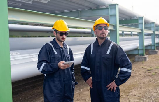 Close up two engineer or factory technician workers stand beside petrochemical gas pipeline and use tablet to discuss about their work.