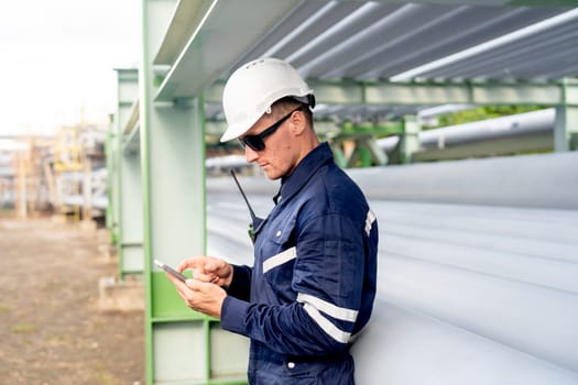 Side view of engineer or technician worker leaning against the petrochemical pipeline and enjoy with his mobile phone.