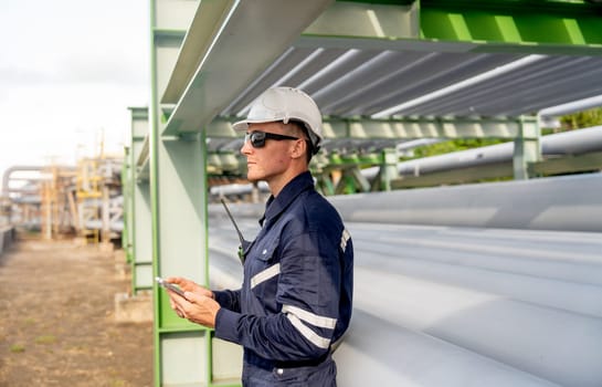 Wide and side view of engineer or technician worker leaning against the petrochemical pipeline and enjoy with his mobile phone.