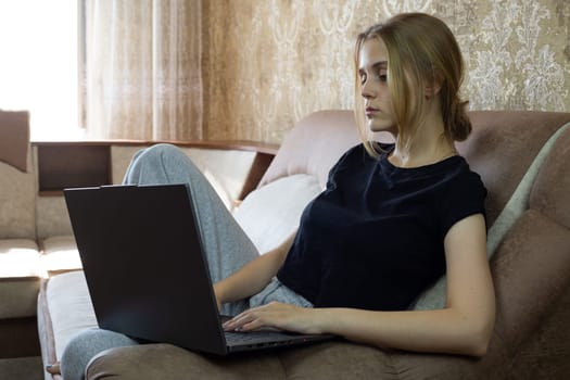 Young woman is focused on her laptop while relaxing at home, highlighting remote work and comfort