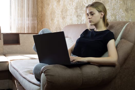 Young woman is deeply focused on her laptop while comfortably relaxing on stylish sofa in modern living room