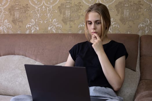 Young woman is deeply and thoughtfully engaging with her laptop in cozy, warm, and inviting home setting