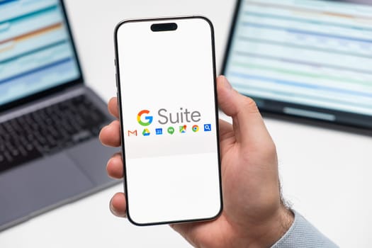 PRAGUE, CZECHIA - JULY, 2024: Google Suite logo on the screen of smartphone in mans hand and laptop on the background