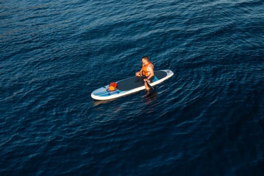A tourist on a paddleboard enjoys the pristine beauty of the azure sea, aerial view