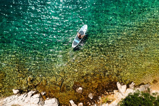 Top view of woman navigates SUP in the tranquil clear water.
