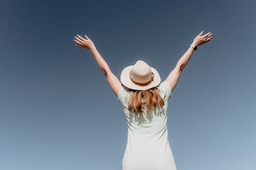 A woman wearing a straw hat stands with her arms raised against a clear blue sky, suggesting joy and freedom.
