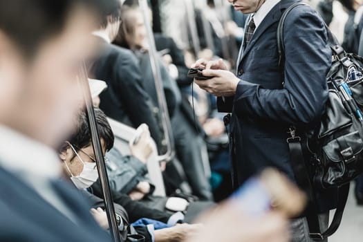 Interior of modern Tokyo metro with passengers on seats and businessmen using their cell phones. Corporate business people commuting to work by public transport. Horizontal composition.