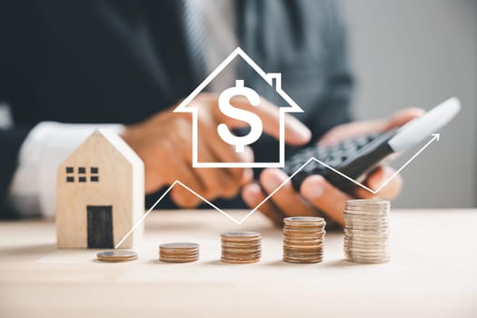 Hand presses calculators, planning home refinance. House model, buy or rent note, calculators on desk. Concept of saving to buy property payment. Tax, credit analysis for better financial future.
