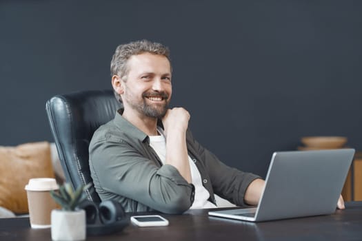 Smiling man finds joy in work as he diligently operates laptop on well-organized desk within bustling office environment. Corporate world, where he excels in his career with sense of fulfillment. High quality photo