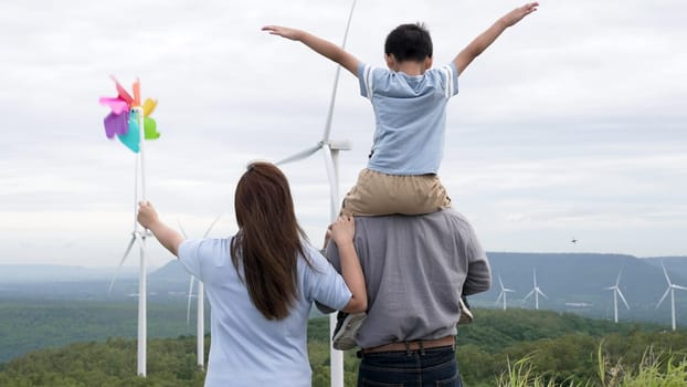Concept of progressive happy family enjoying their time at the wind turbine farm. Electric generator from wind by wind turbine generator on the country side with hill and mountain on the horizon.