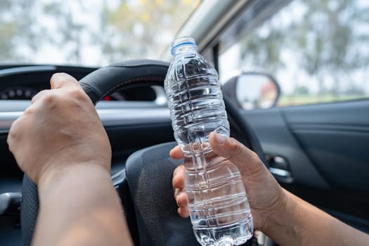 Asian woman driver holding bottle for drink water while driving a car. Plastic hot water bottle cause fire.