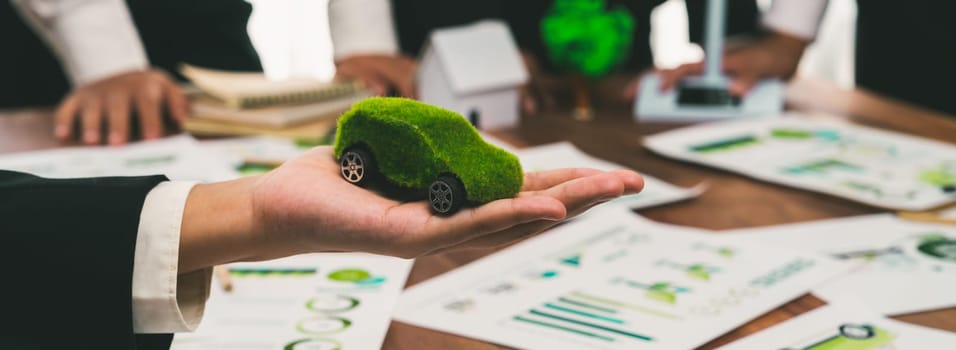 Businessman holding green EV car model mock in electric car company meeting, business people planning strategic marketing for eco-friendly vehicle product using clean energy with net zero.Trailblazing