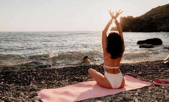 Young woman in swimsuit with long hair practicing stretching outdoors on yoga mat by the sea on a sunny day. Women's yoga fitness pilates routine. Healthy lifestyle, harmony and meditation concept.