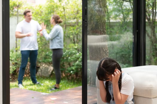 Stressed and unhappy young girl huddle in corner, cover her ears blocking sound of her parent arguing in background. Domestic violence at home and traumatic childhood develop to depression. Synchronos