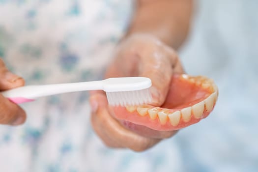 Asian elderly woman patient use toothbrush to clean partial denture of replacement teeth.