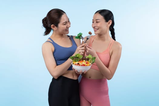 Two young sporty Asian women in sportswear holding salad bowl fill with fruit and vegetable. Natural youthful and fit body lifestyle people with balance nutrition on isolated background. Vigorous