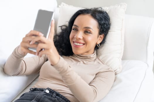 Relaxed young African American woman using crucial mobile phone on sofa couch in living room at home