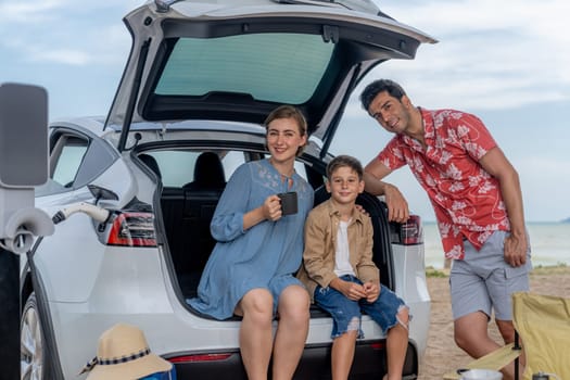 Family vacation trip traveling by the beach with electric car, happy family recharge EV car, enjoying outdoor camping coffee. Seascape travel and eco-friendly car for clean environment. Perpetual