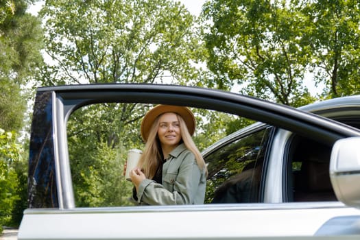 Smiling young woman drinking coffee or tea from reusable thermos cup. Traveler making a coffee break in Local solo travel on weekends concept. Exited woman explore freedom outdoors in forest. Unity with nature lifestyle, rest recharge relaxation