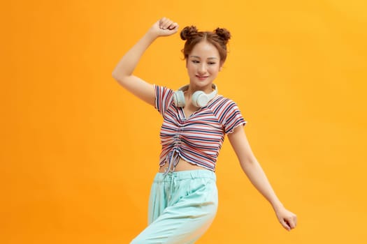 Girl dancing on yellow background wearing headphones on neck, lifestyle concept, copy space