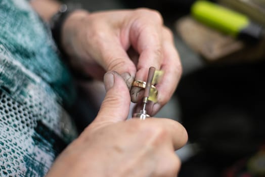 Goldsmith polishing a gold ring jewel in his jewelry workshop. Jeweler hands working in his craftwork studio. High quality photo