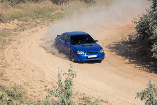 Sunny summer day. A blue rally car makes a sharp turn on a dirt track