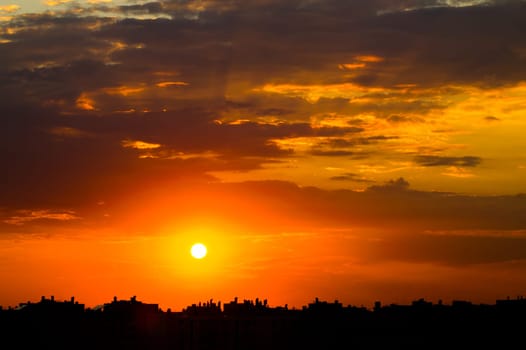 Cloudy sky over the city rooftops. Bright sunset over the silhouettes of buildings