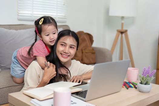 A mother and her young daughter share a joyful moment while working from home on a laptop in a comfortable living room.