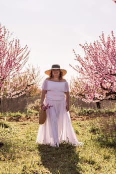 Woman blooming peach orchard. Against the backdrop of a picturesque peach orchard, a woman in a long white dress and hat enjoys a peaceful walk in the park, surrounded by the beauty of nature