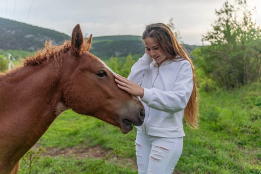 A woman is petting a brown horse in a field. Scene is peaceful and calming