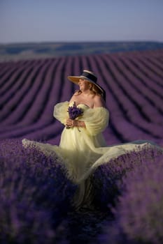 Woman poses in lavender field at sunset. Happy woman in yellow dress holds lavender bouquet. Aromatherapy concept, lavender oil, photo session in lavender.