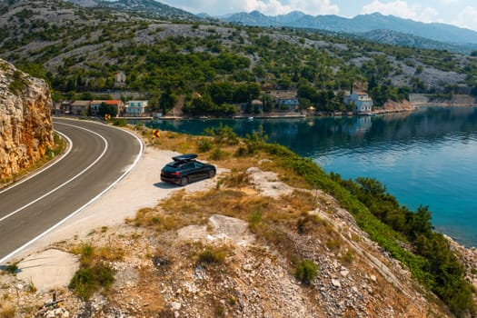 Aerial view of car with a roof box stands on the side of a cliff and beautiful rocks in the background