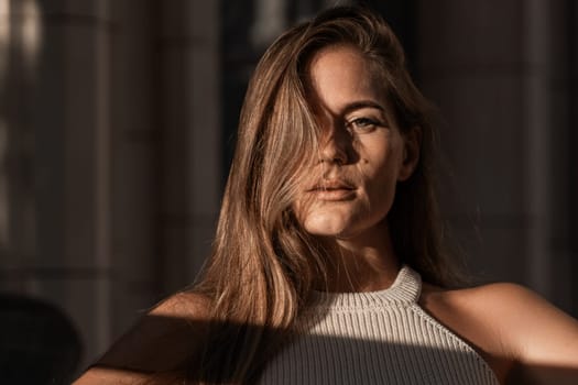 A woman with long brown hair looks intensely at the camera, her face partially obscured by her hair. The light casts a shadow across her face and body.