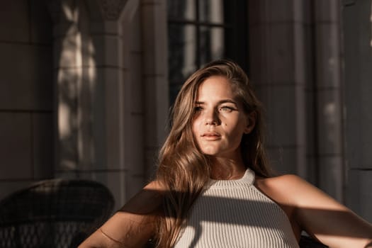 A woman with long brown hair sits in a chair, bathed in sunlight streaming through a window. She looks directly at the camera with a serious expression.